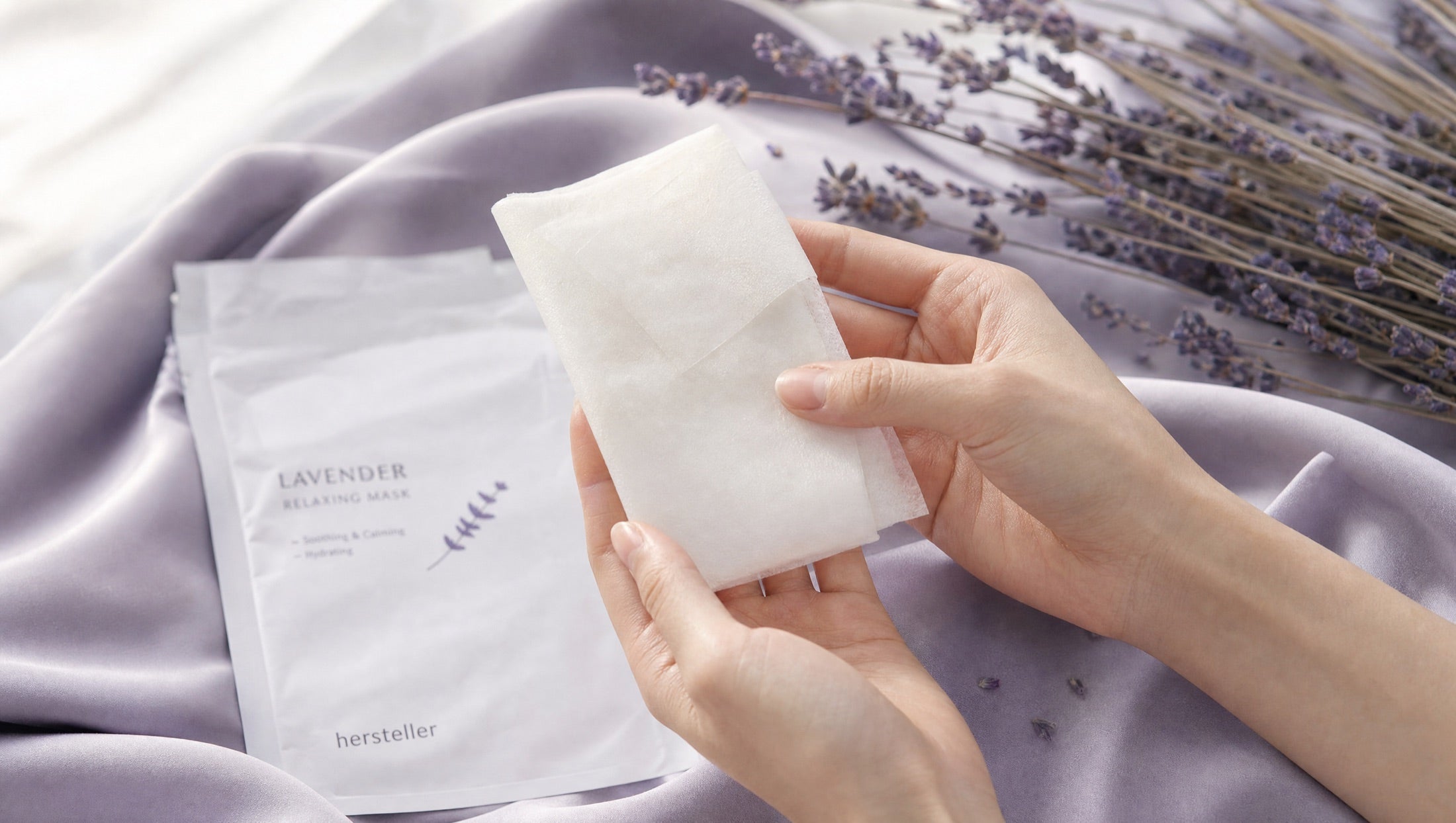 Hands holding a Serica mask sheet on lavender silk